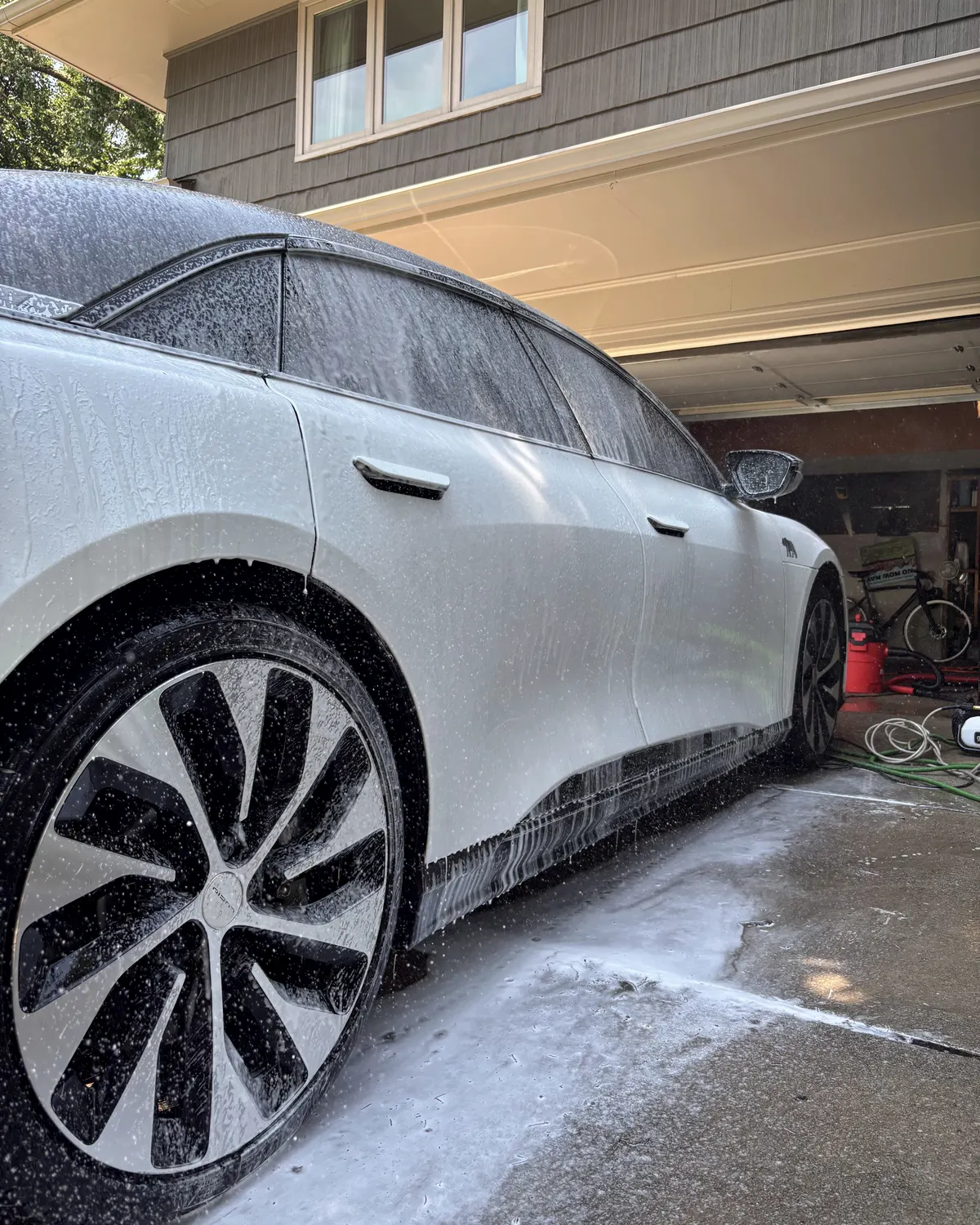 White Lucid Air covered in snow foam in front of an open home garage