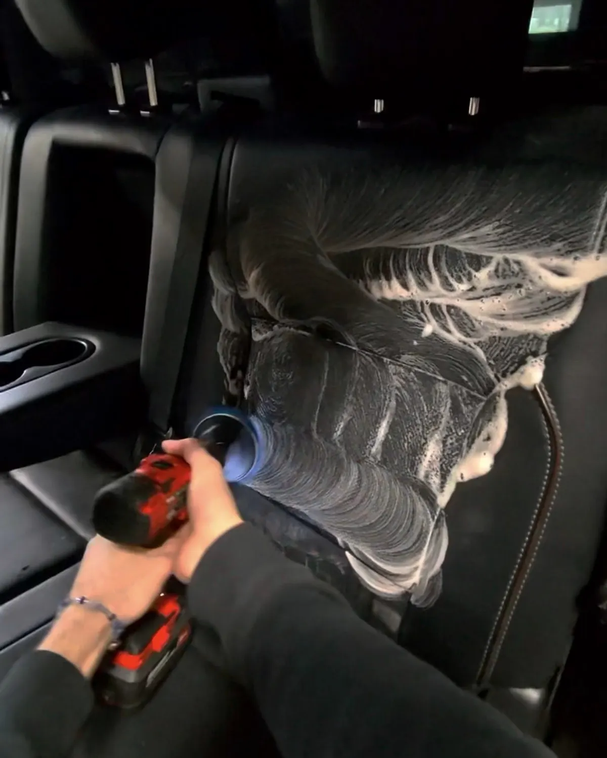 Spinning drill brush working foam into a black rear seat