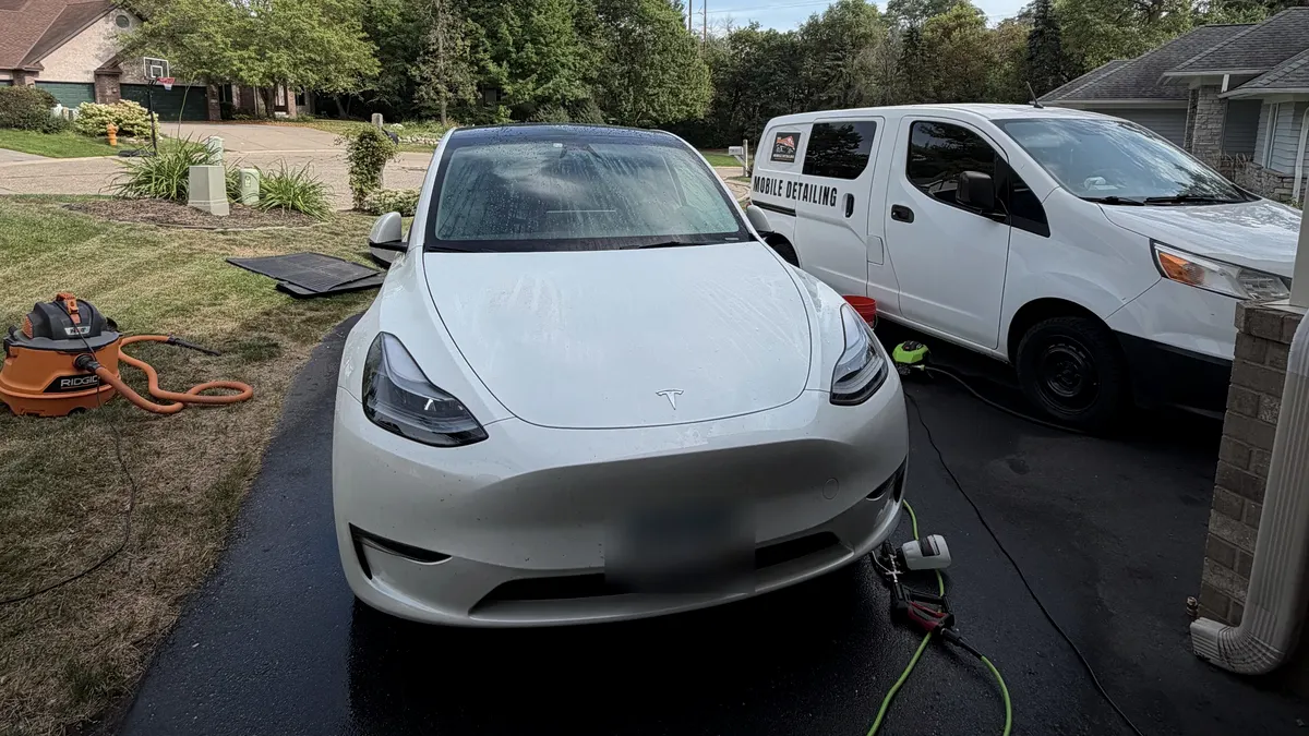 White Tesla Model Y in a driveway beside the white detailing van, hoses and a vacuum laid out